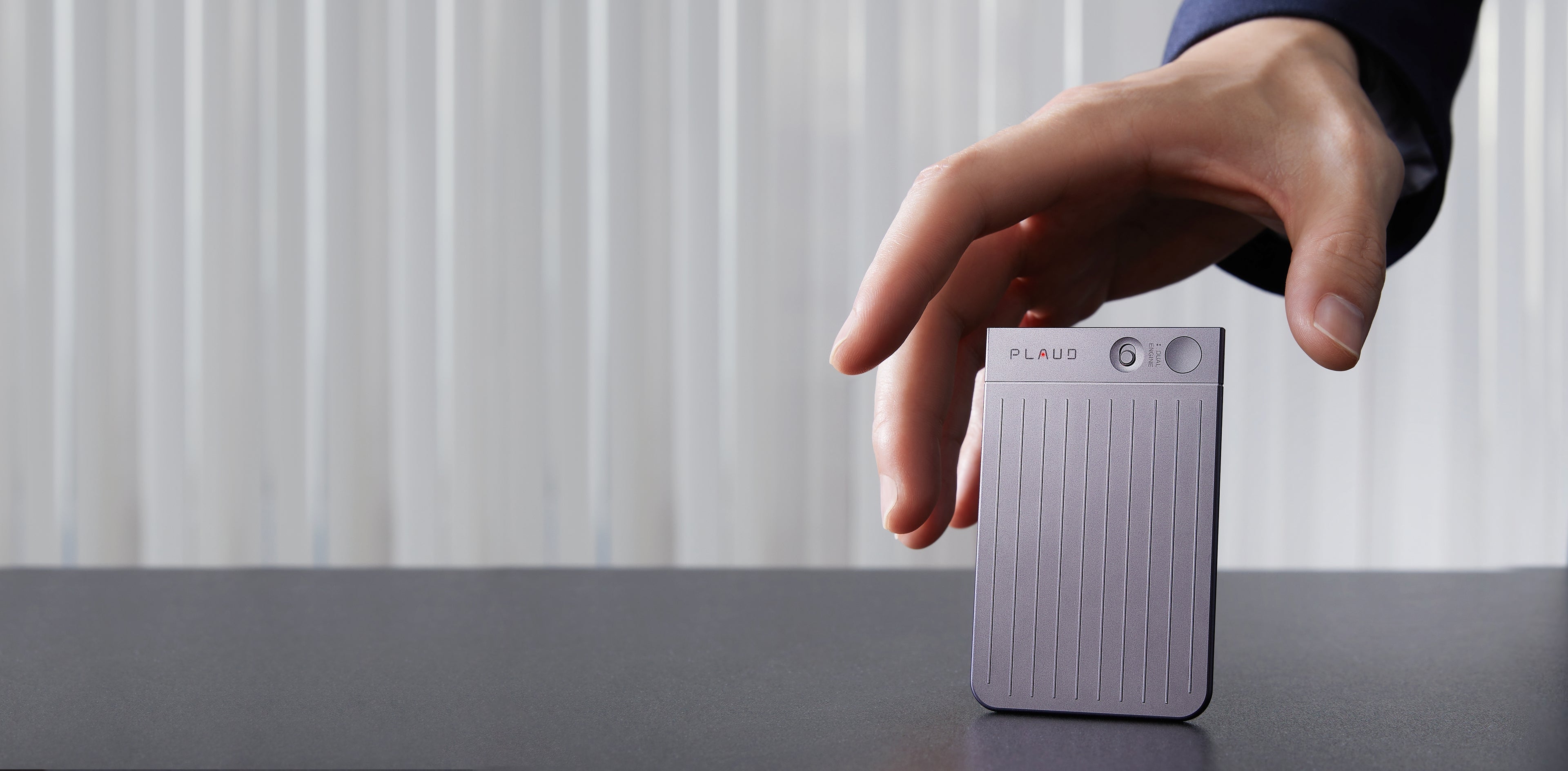 A hand reaches to pick up a Starlight Plaud Note AI voice recorder from a dark desk.