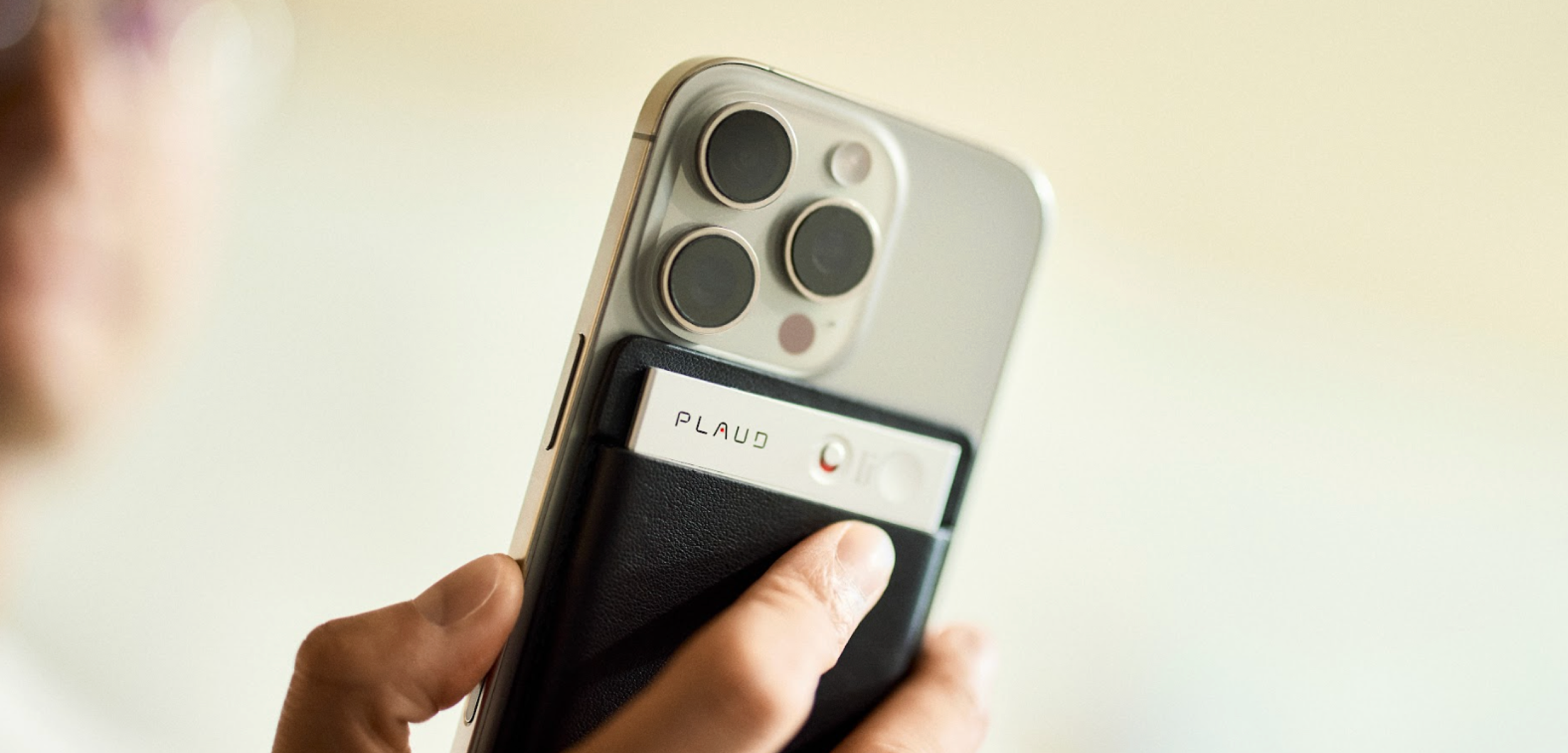 Silver Plaud Note attached to an iPhone in a black case, with a hand pressing the button.