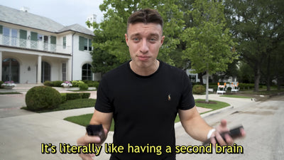 Man holding a black Plaud Note and phone. Text: 'It's literally like having a second brain.'