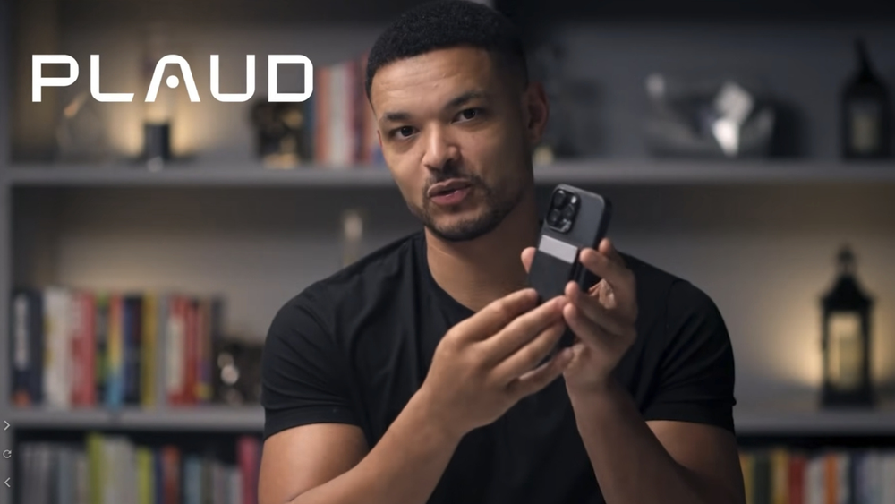 Man holding a silver Plaud Note attached to the back of a smartphone.