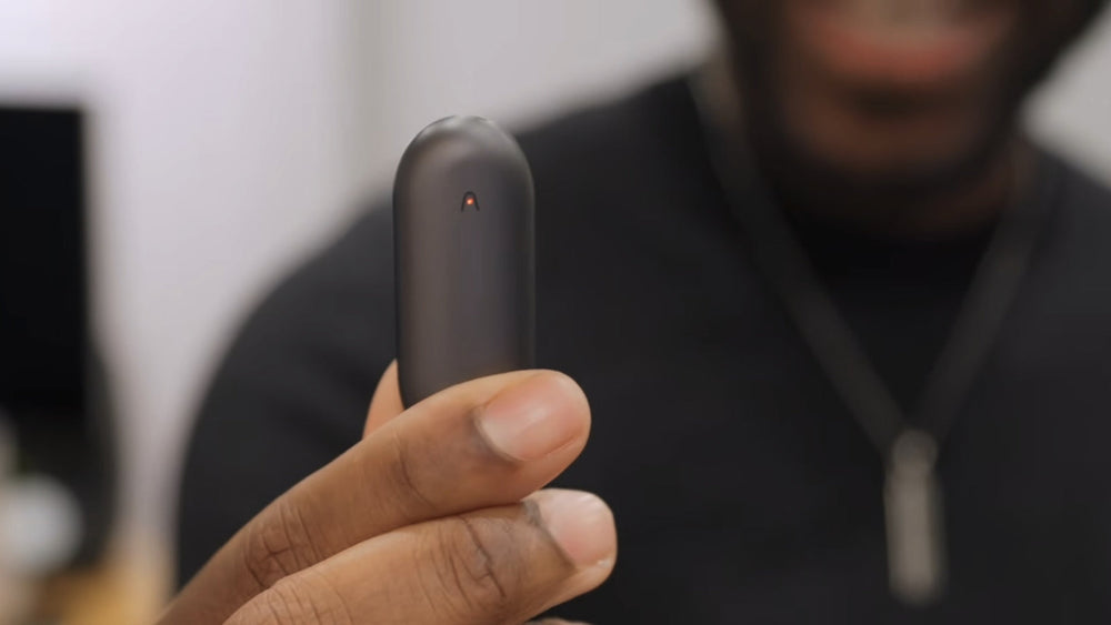 A person holds a Cosmic Gray Plaud NotePin AI voice recorder between their fingers.