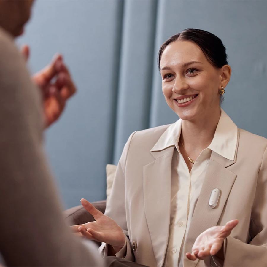 Woman wearing a silver Plaud NotePin on her blazer lapel during a conversation.