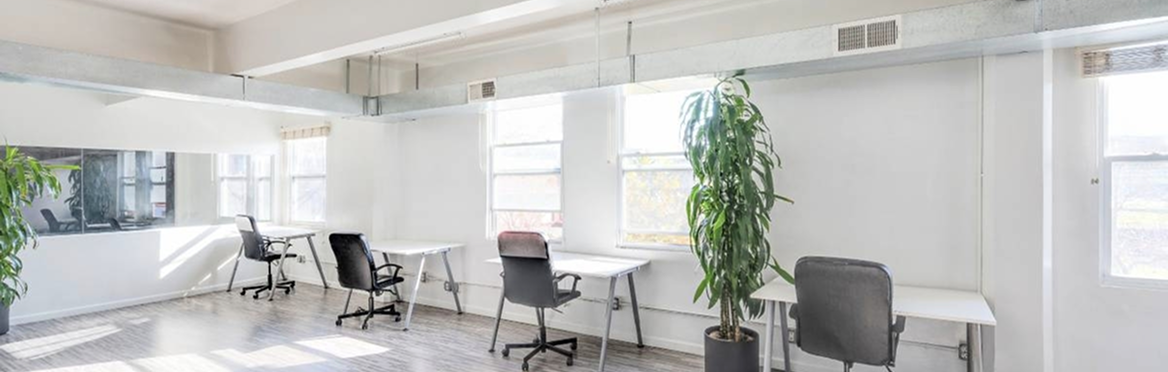 Bright, modern open-plan office space with white desks, black chairs, and natural light from large windows.