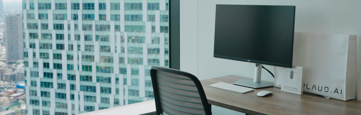 Modern office desk featuring a Plaud NotePin box and Plaud.ai shopping bag by a window with city views.