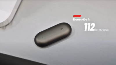 Dark gray Plaud NotePin on a desk with text stating it transcribes in 112 languages.