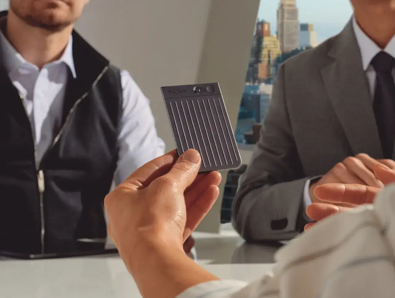 Person holds a black Plaud Note during a business meeting in a professional office setting.