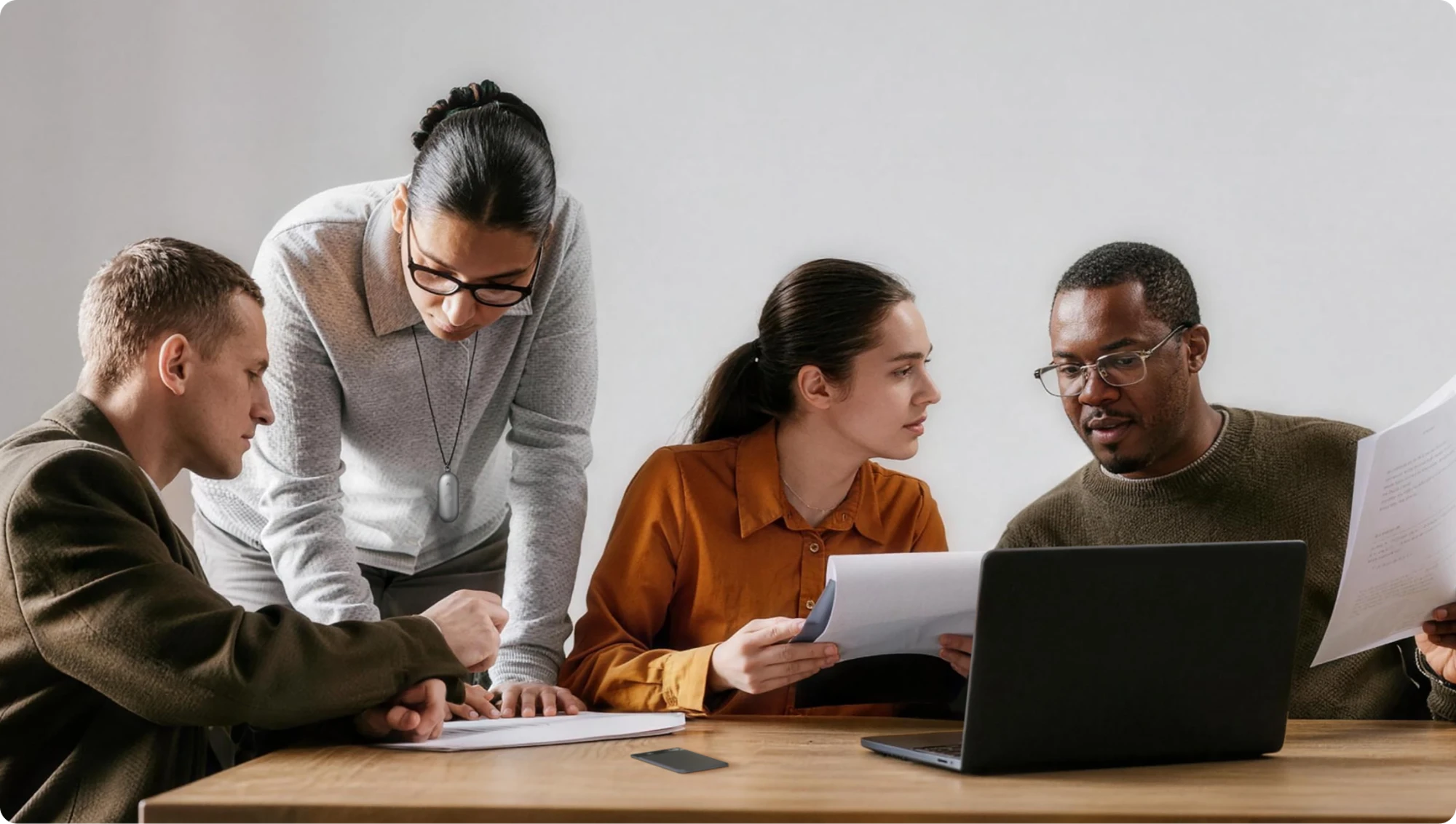Professionals collaborating at a desk; a woman wears a silver Plaud NotePin on a lanyard.