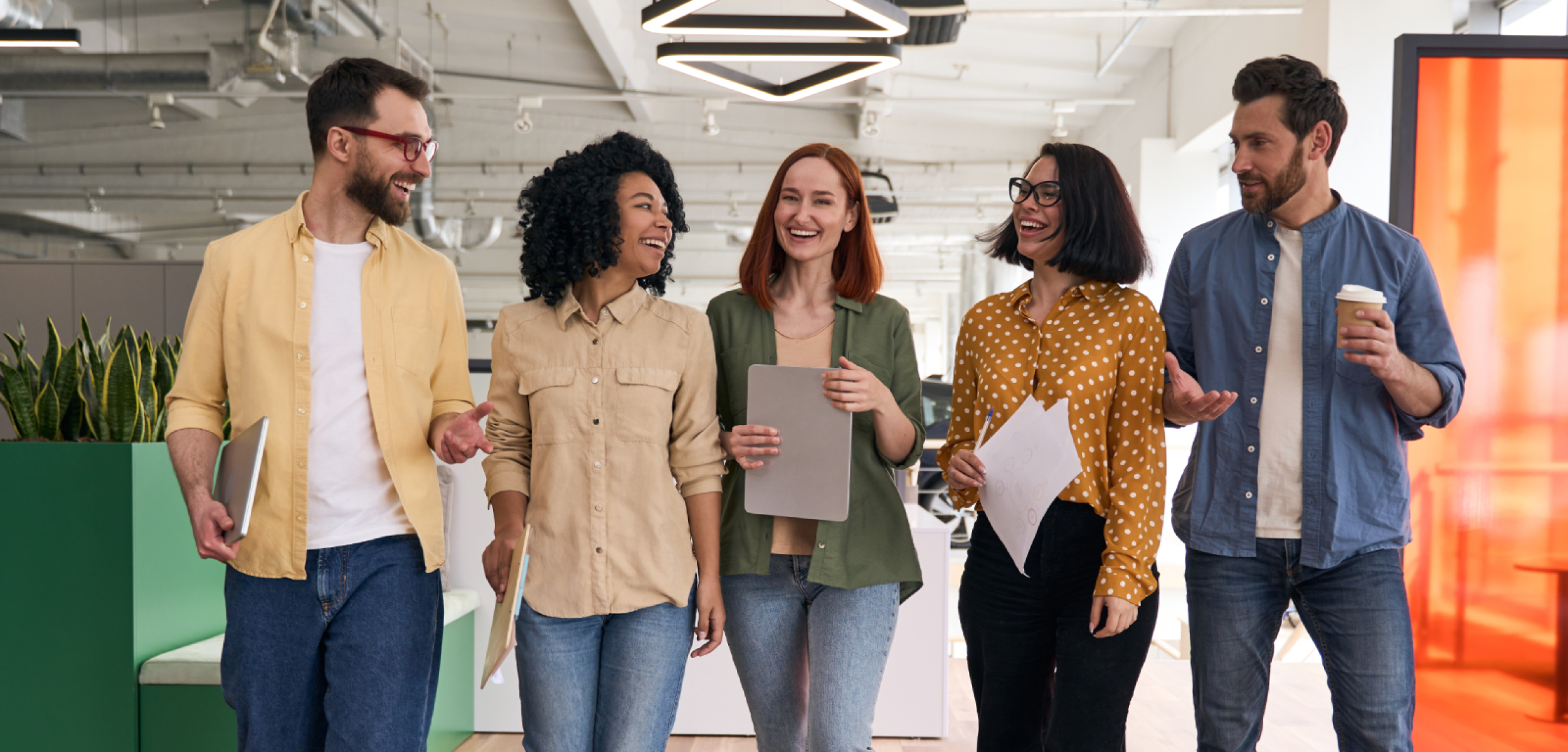 A diverse group of smiling professionals walking and collaborating in a bright, modern office.